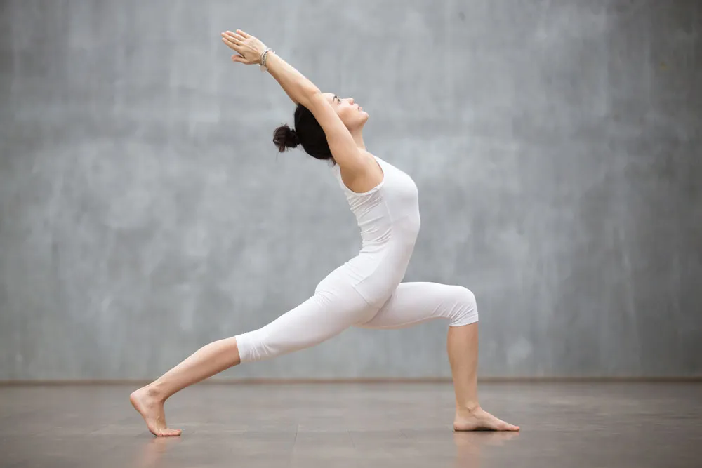 woman in white outfit doing yoga pose on floor with gray wall