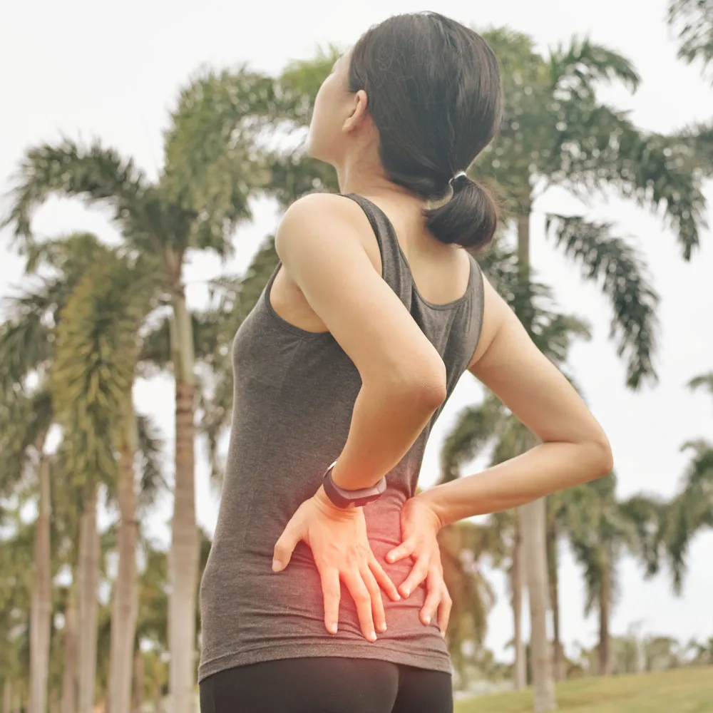 woman with back pain in park with palm trees in background